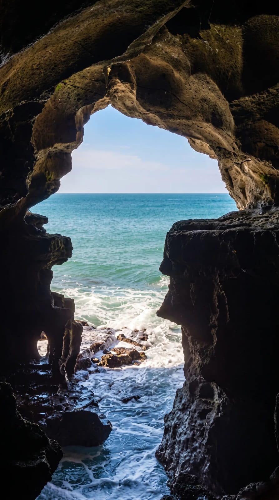 Uma vista próxima e frontal através da abertura em forma de mapa de África nas Grutas de Hércules, com ondas a rebentar nas rochas em baixo